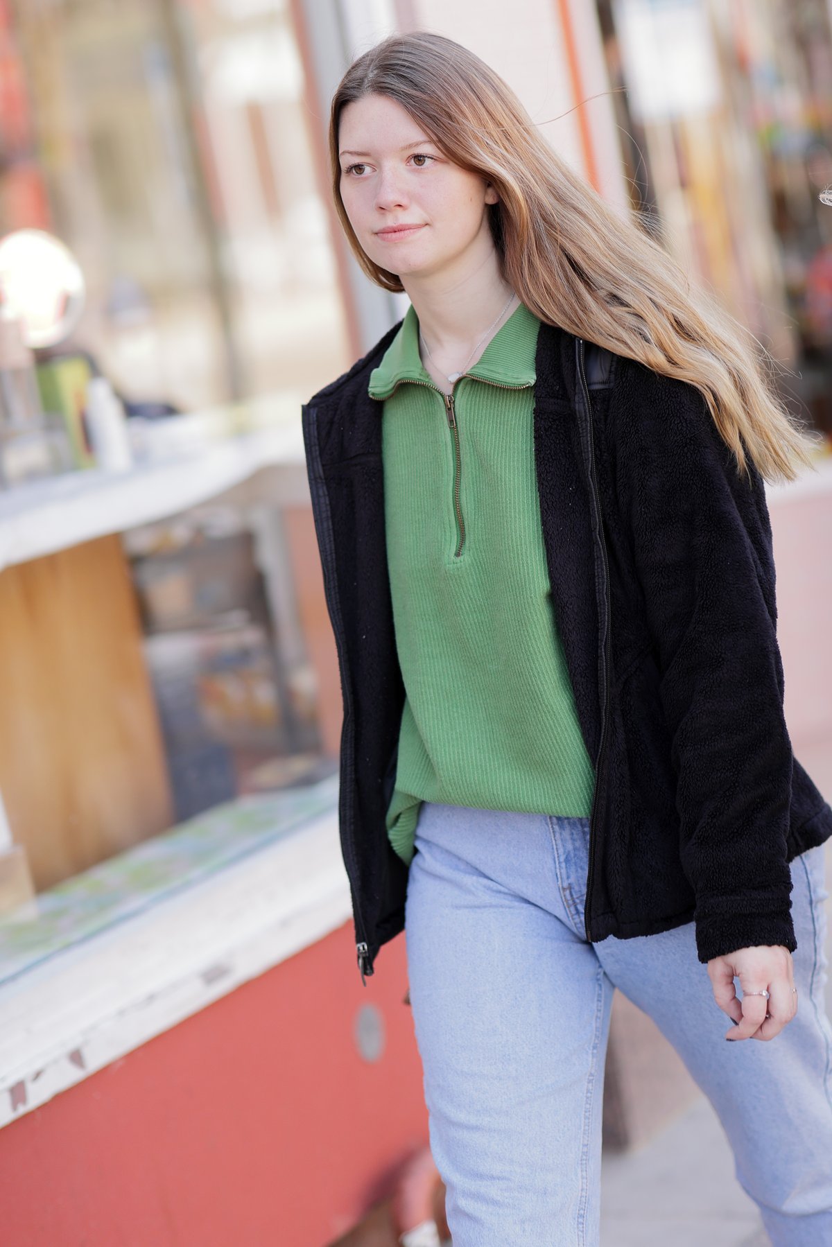 Woman in a black jacket, green polo shirt and light-wash jeans on a city street