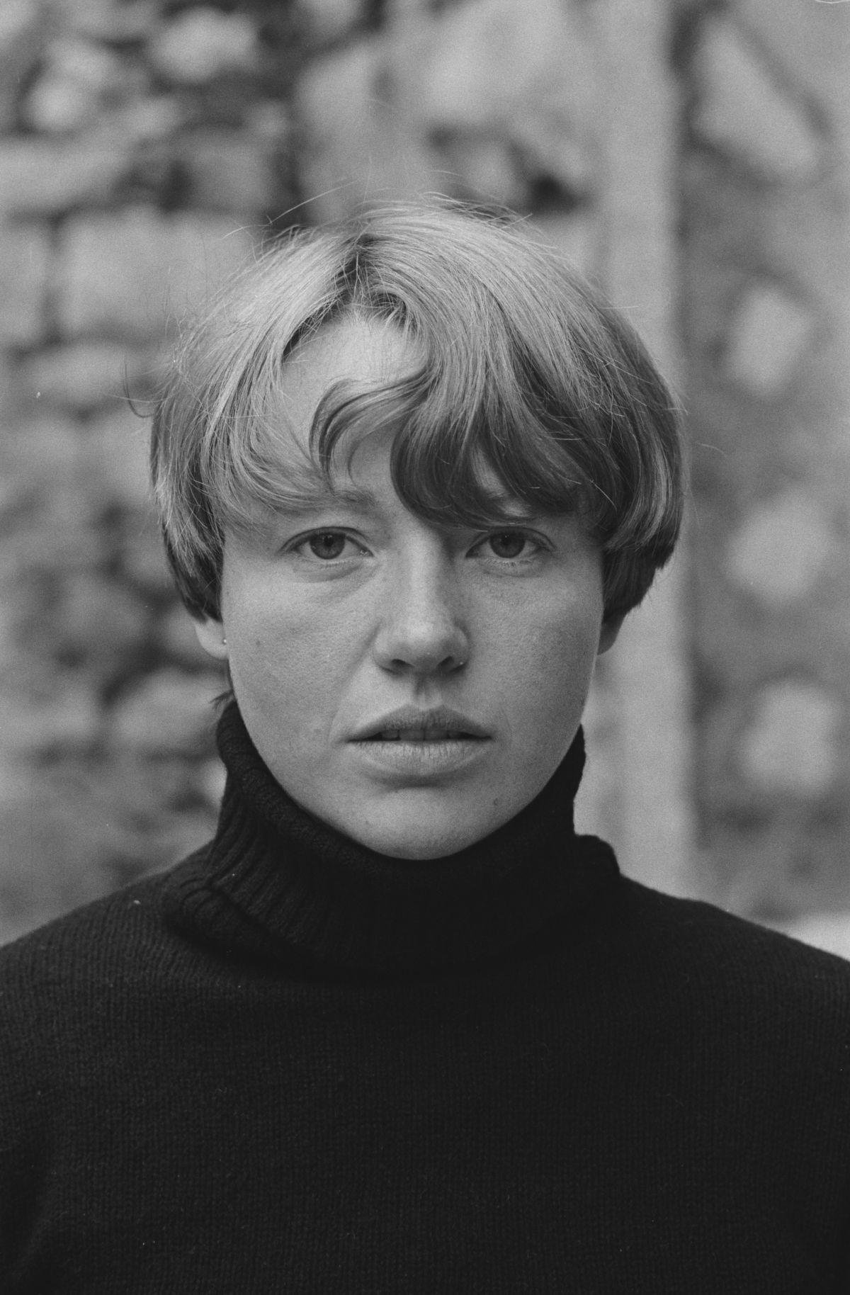 Black-and-white vintage close-up portrait of a young woman with a short blonde bob wearing a black ribbed polo-neck jumper, the high turtleneck collar prominent around her neck.
