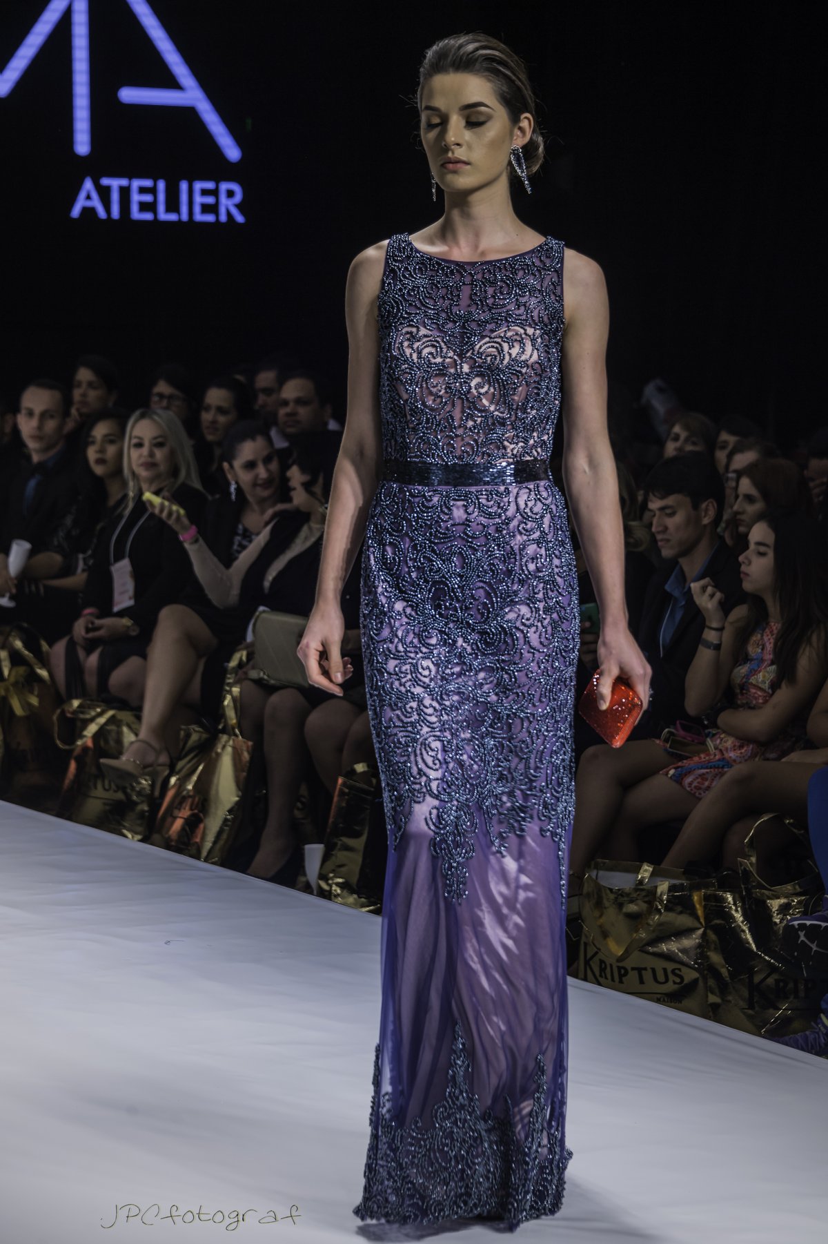 Model wearing a deep blue lace evening gown and carrying a small red clutch