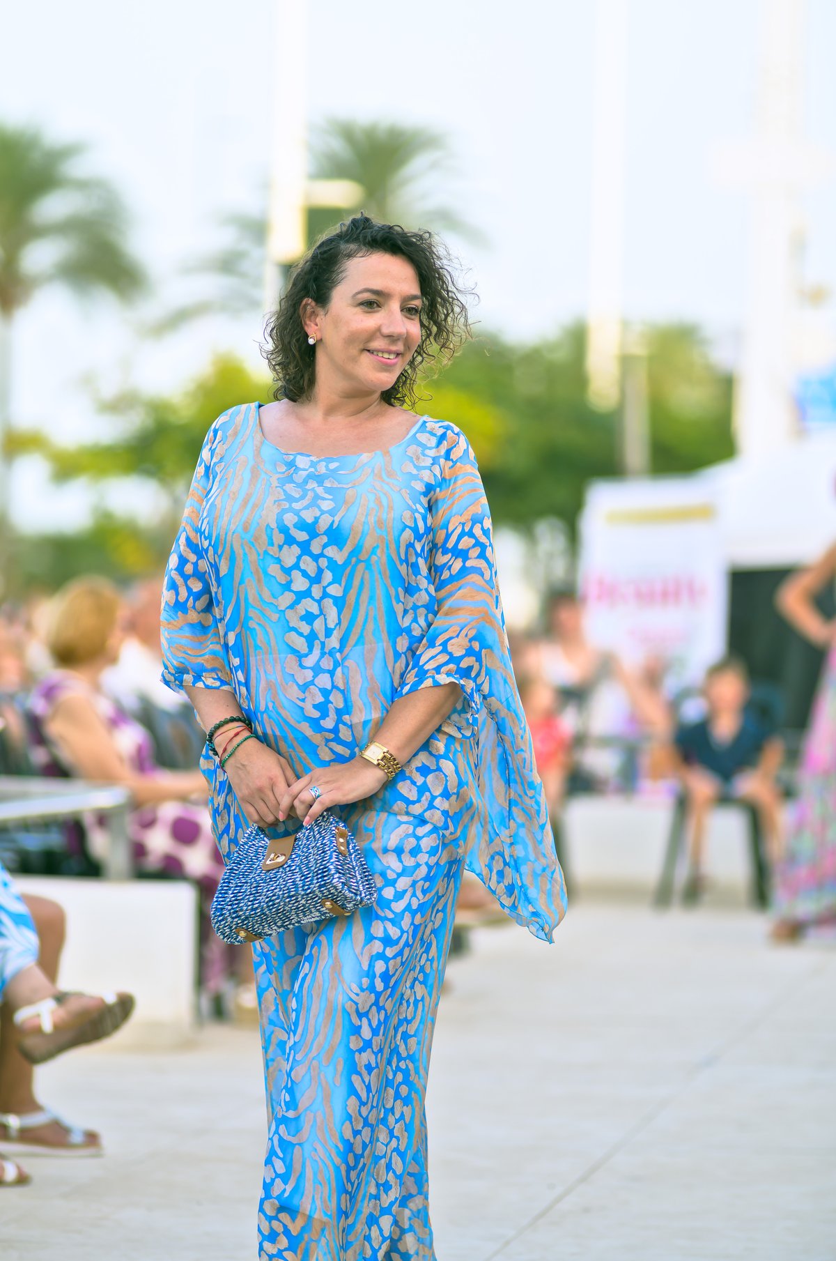 Woman in a blue lace outfit holding a matching blue clutch bag at an outdoor daytime event