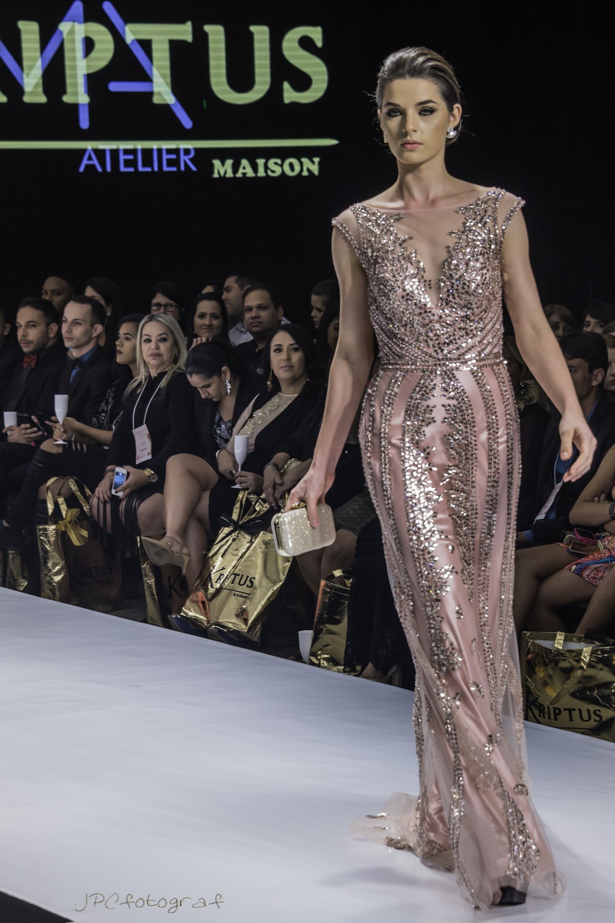 Model wearing a blush pink full-length sequined gown with a plunging illusion neckline