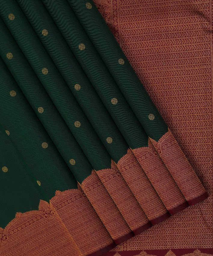 Folded dark green silk saree with gold zari dots and a wide maroon and gold woven border
