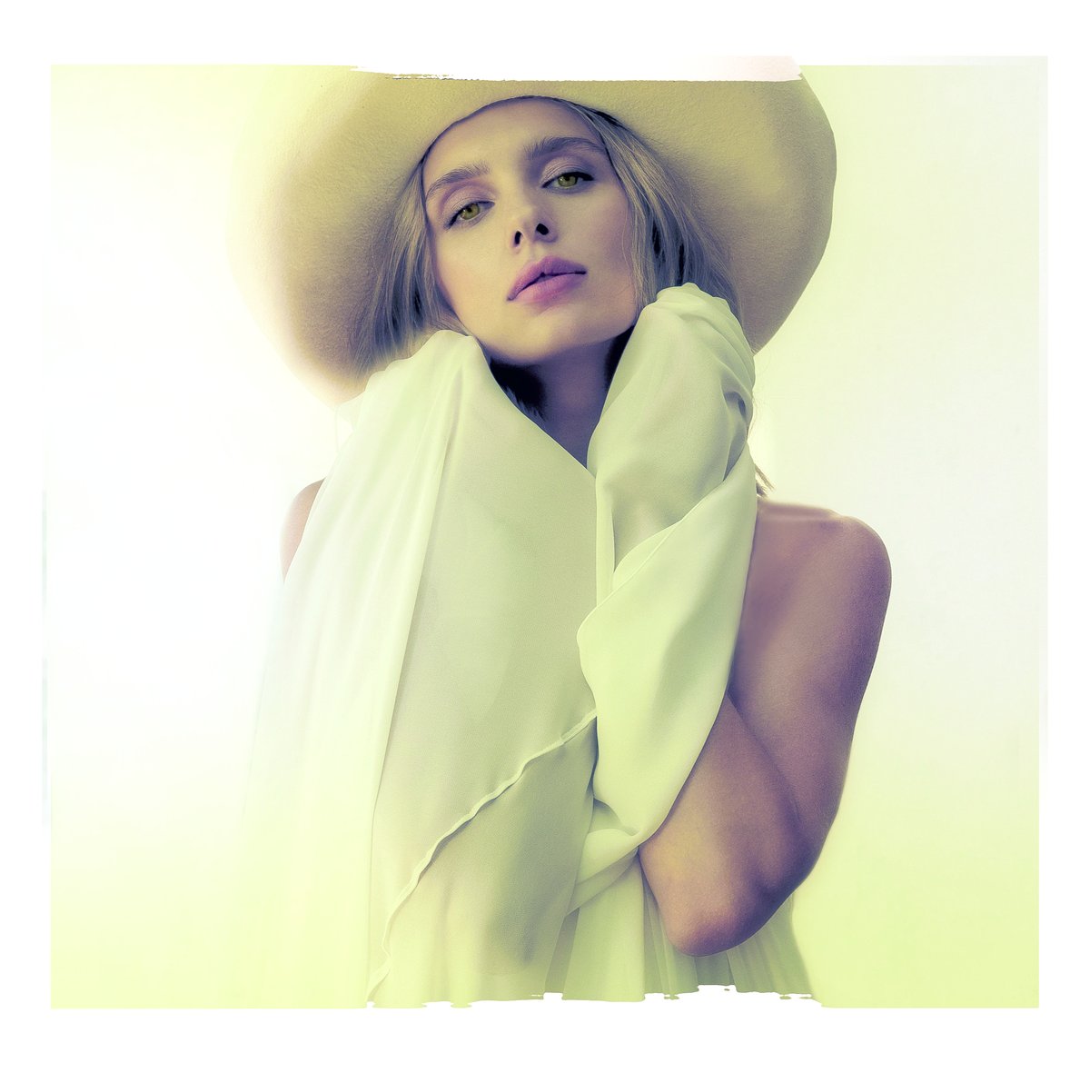 Woman in a pale cream-yellow flowing blouse and wide-brim hat, soft fashion portrait