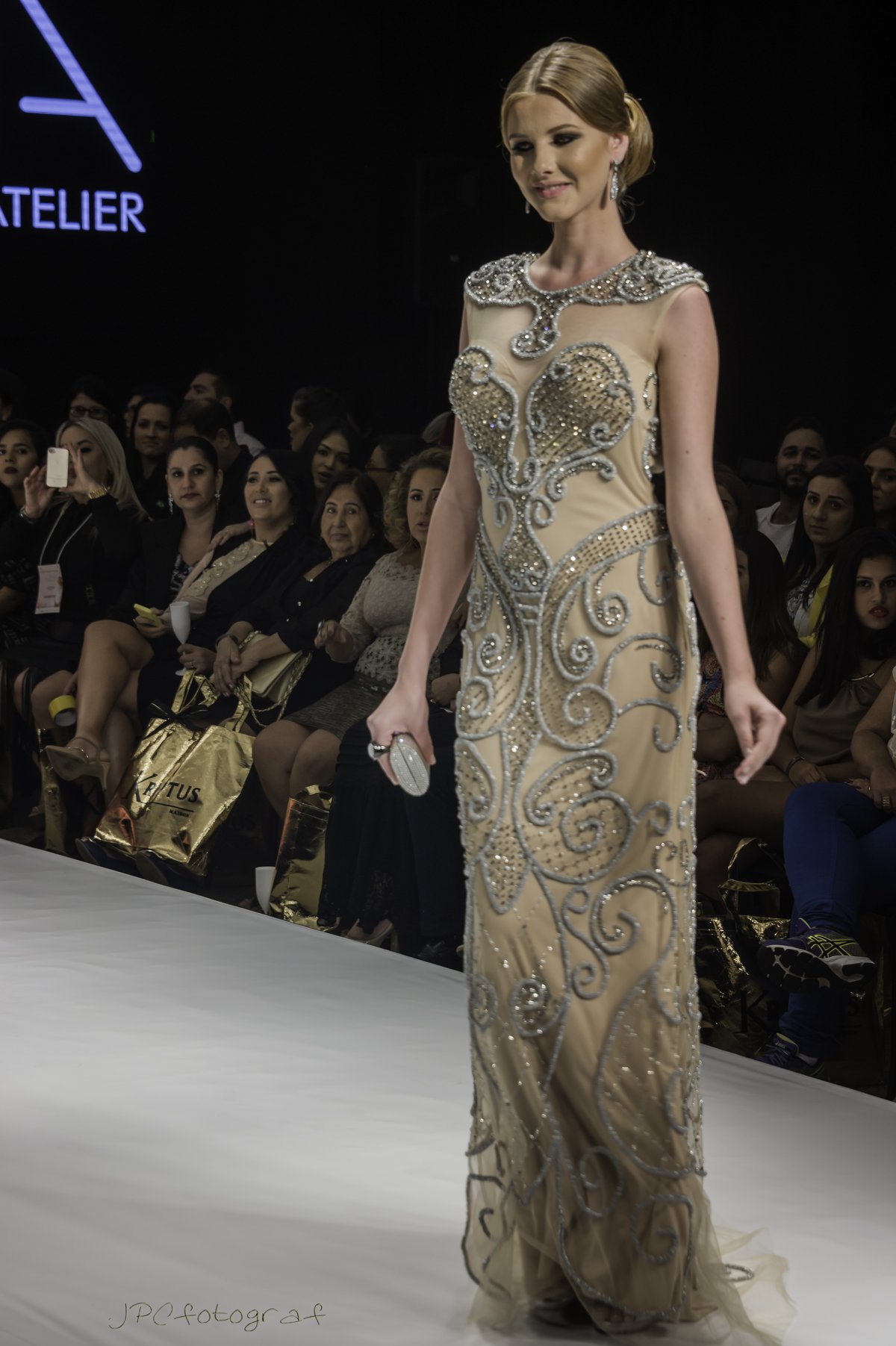 Model wearing a champagne floor-length gown with dense gold and silver beadwork at a fashion show