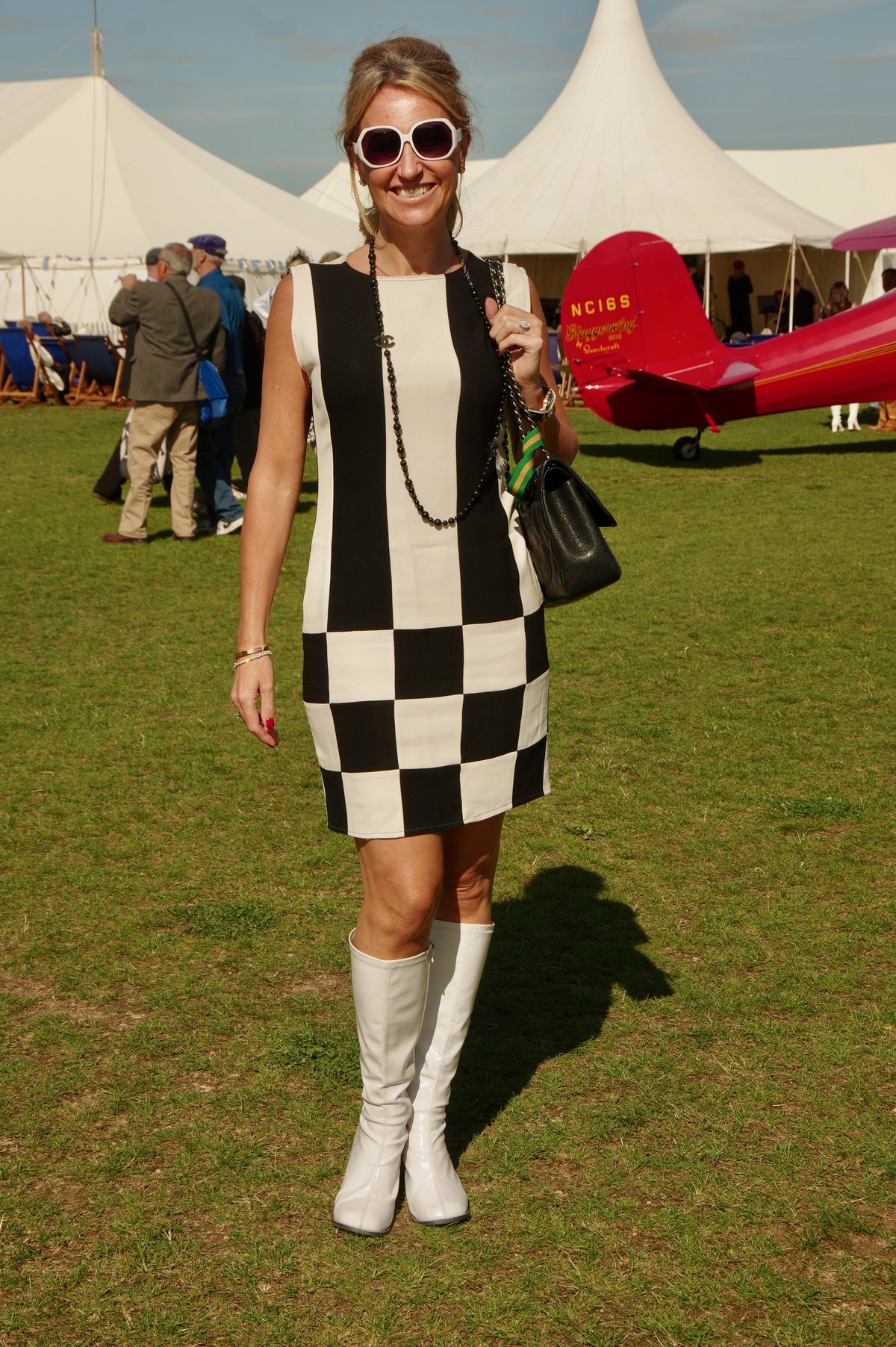 Woman in a black-and-white checkered mini dress and white knee-high boots on grass