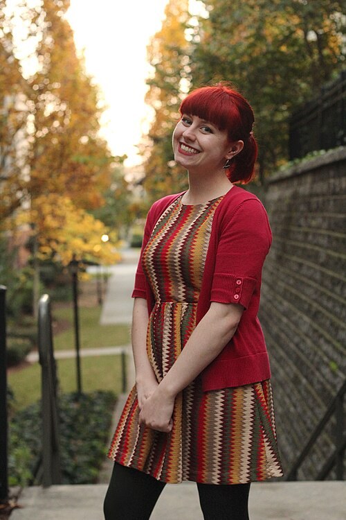 Woman in a chevron-patterned fit-and-flare dress with a red cardigan standing among autumn trees