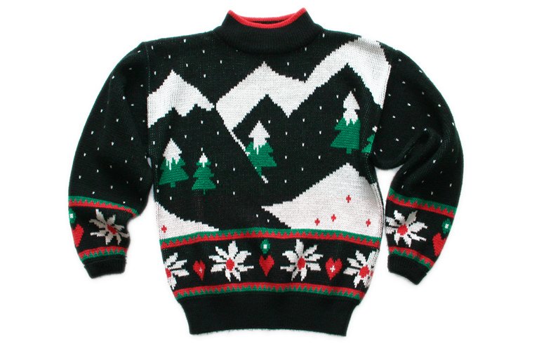 A dark green knitted Christmas sweater with white mountains, green trees and red flowers laid flat