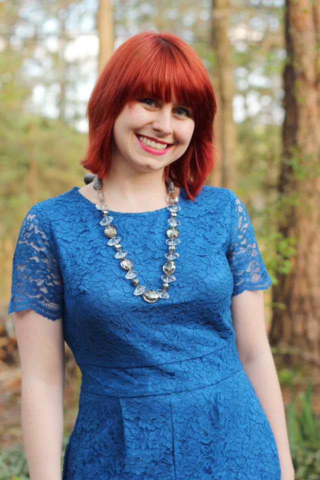 Woman with red hair wearing a cobalt-blue lace dress and a long silver beaded statement necklace