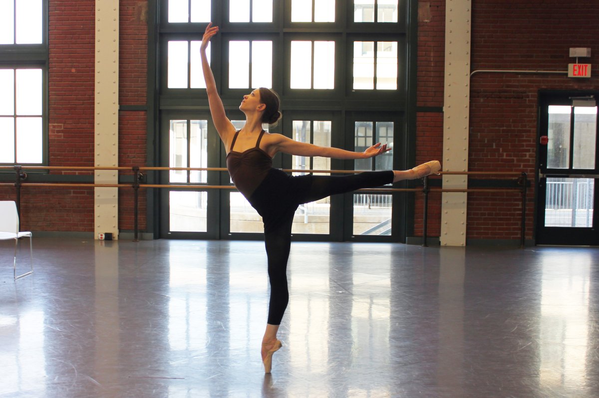 Dancer in a black bodysuit and leggings performing an arabesque