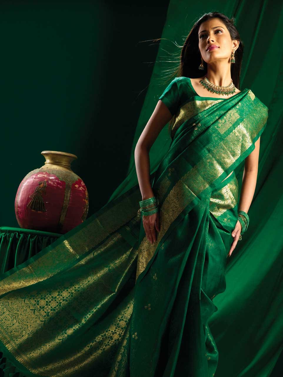Model in an emerald green silk saree with a gold brocade border, wearing green and gold jewellery