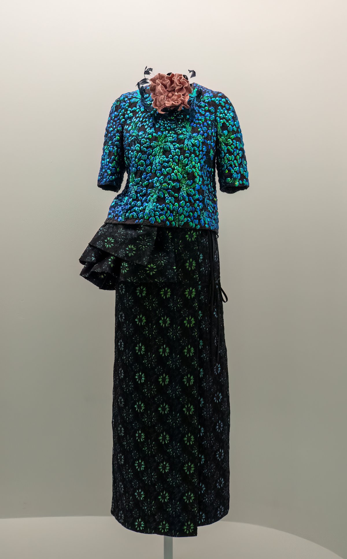 Mannequin wearing a sequined turquoise top with a black floral-embroidered skirt with ruffle detail