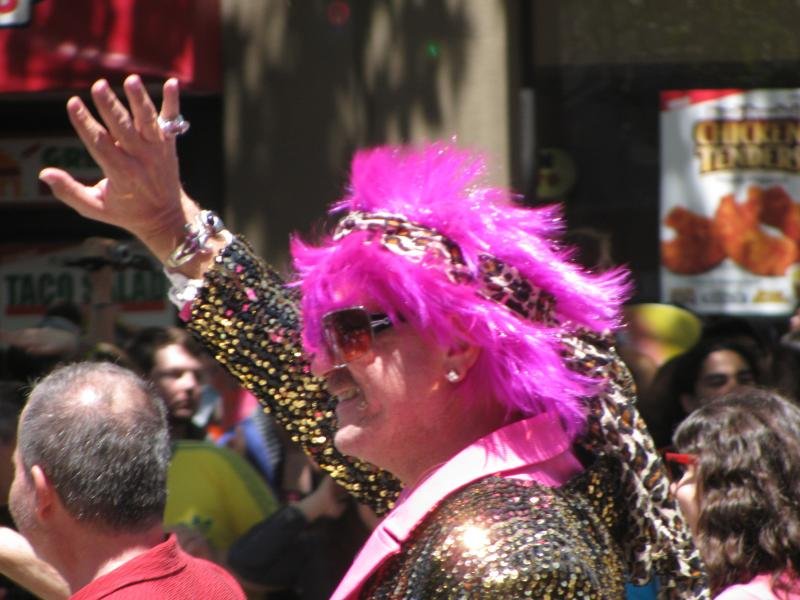 A person with a pink wig wearing a gold glitter sequin coat at a street parade