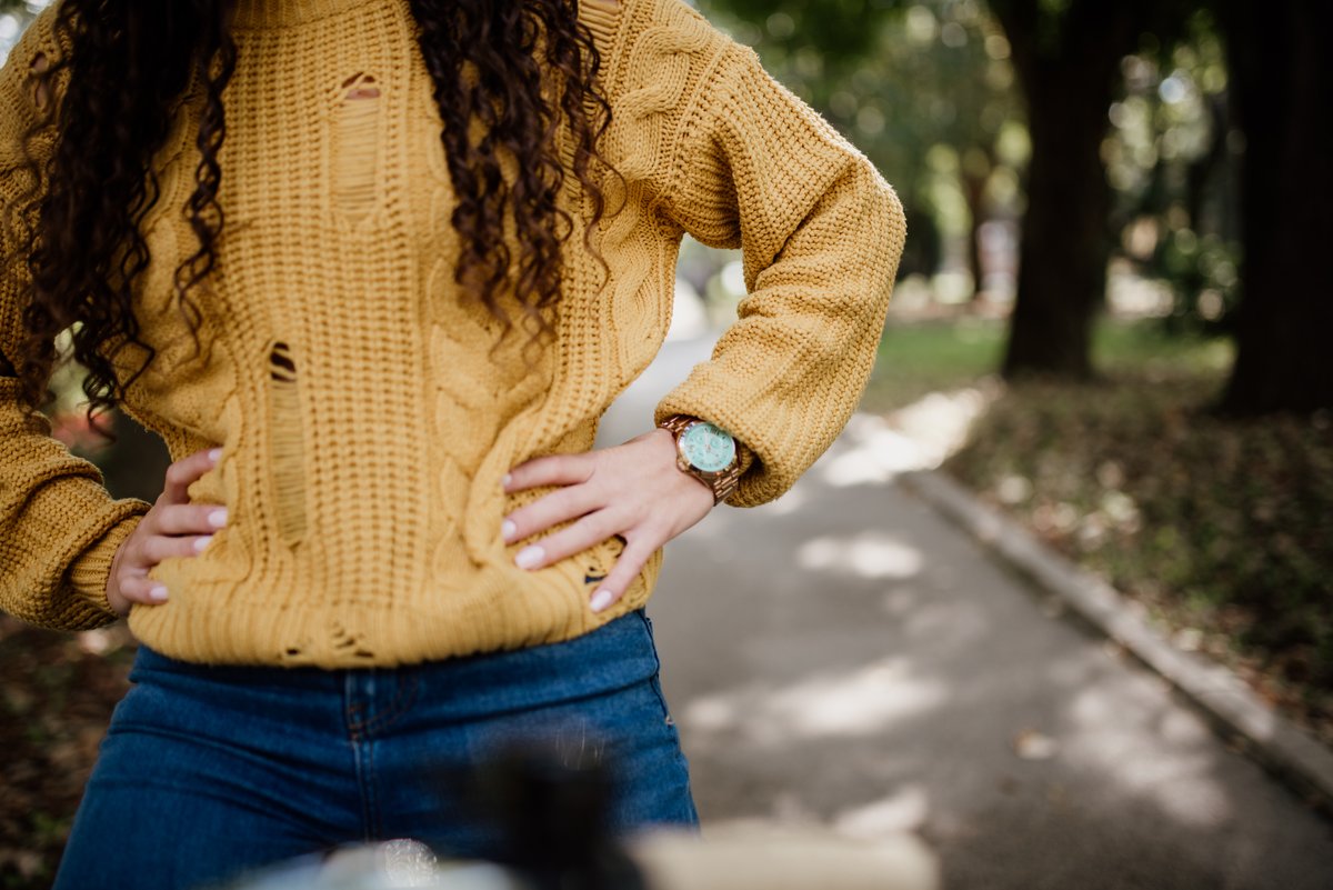 Woman in a golden-mustard chunky knit sweater and blue jeans on a park path