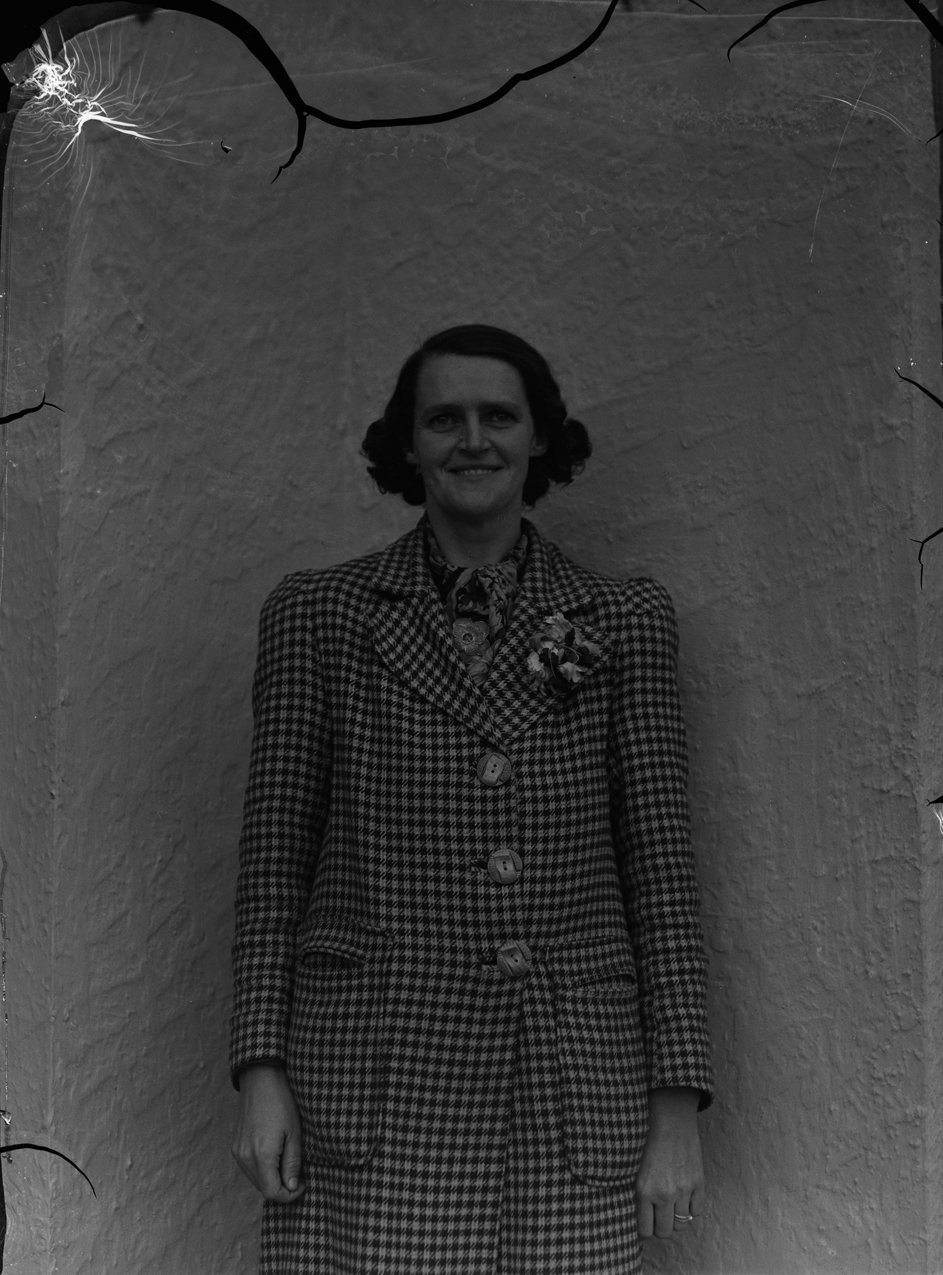 Black-and-white archival portrait of a woman wearing a houndstooth-patterned tweed coat with a floral corsage.