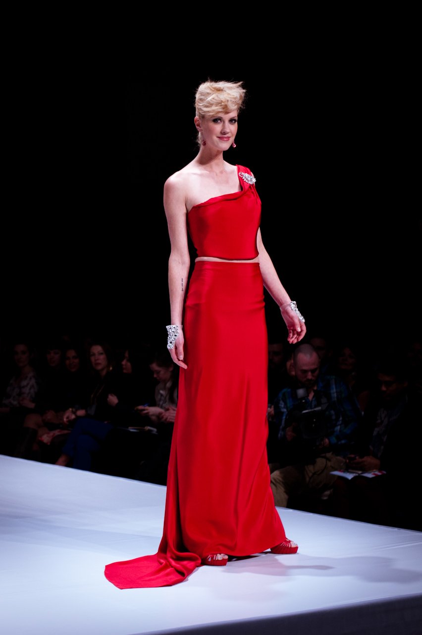 A woman walking on a runway wearing a red one-shoulder floor-length gown