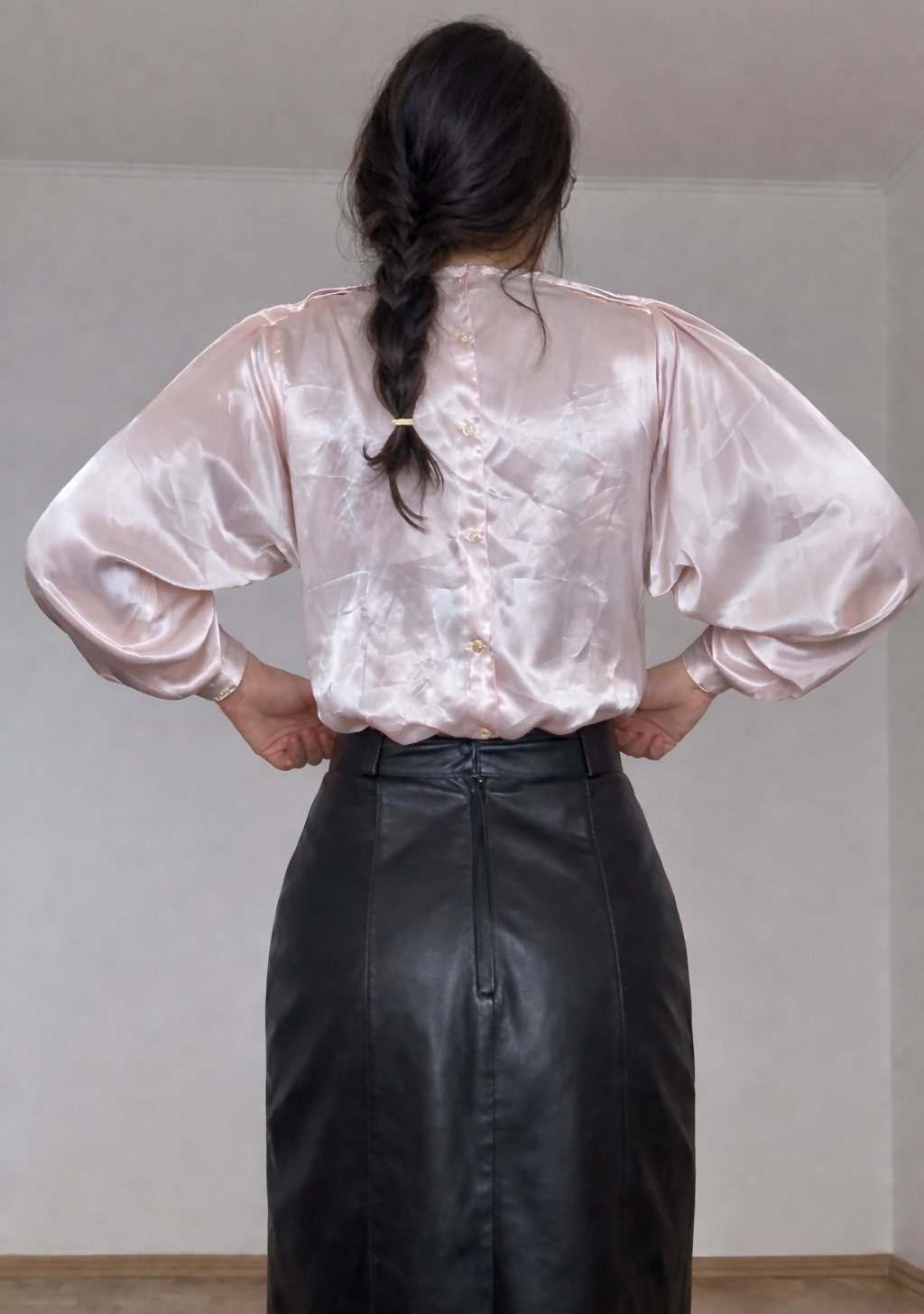 Rear view of a woman wearing a pale pink satin back-button blouse tucked into a black leather pencil skirt