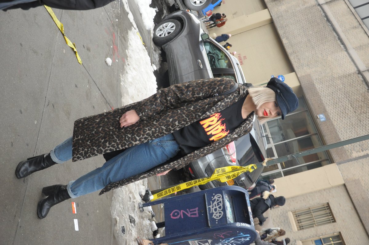 Woman in a leopard-print coat, hat and black boots crossing a street