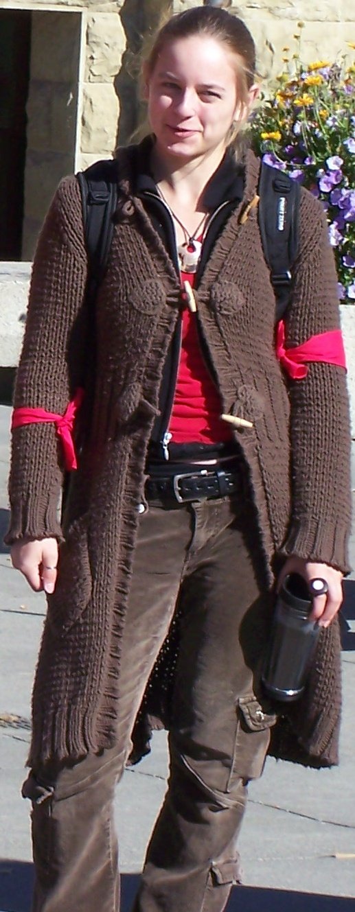 Long brown toggle duster cardigan worn open over a simple red top and dark trousers