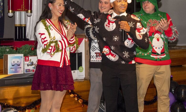A woman wearing a white varsity-style MERRY cardigan, a tinsel garland necklace, a burgundy lace mini skirt, nude tights and gold heels at a holiday party