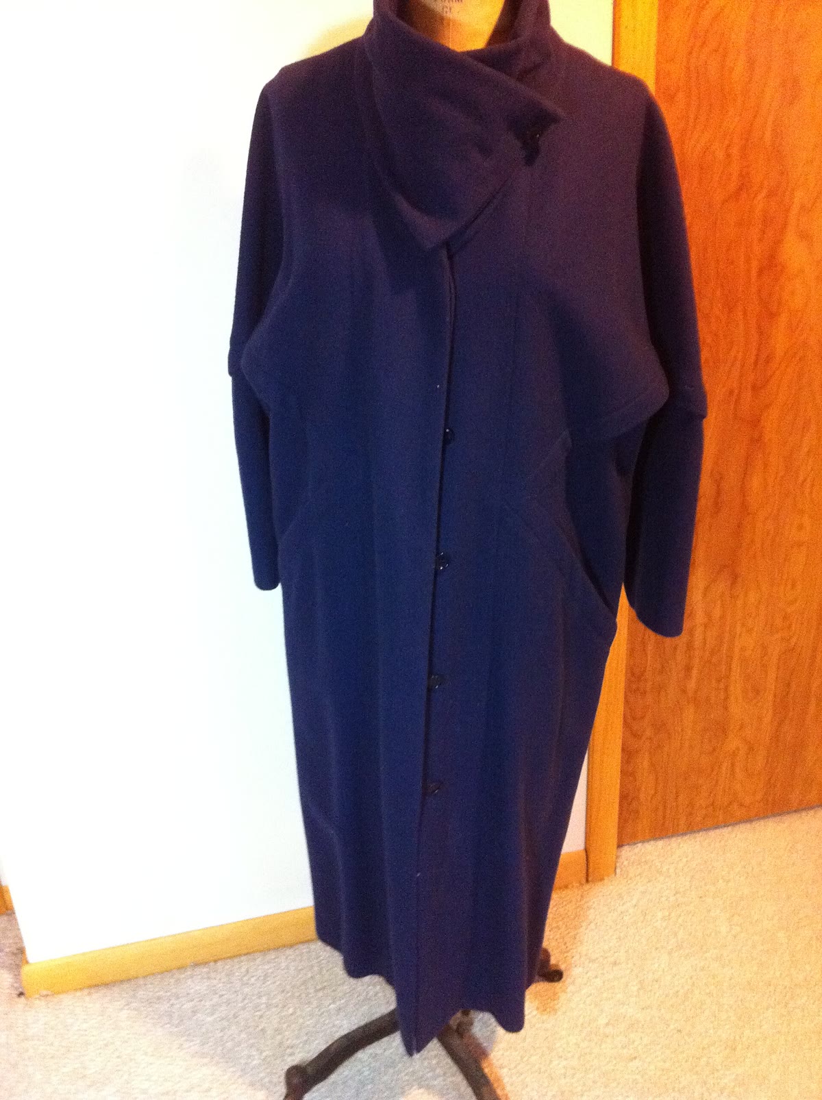 A deep navy women's coat with a draped cowl neckline displayed on a dress form indoors