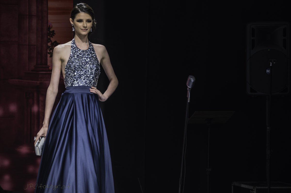 Model wearing a navy halter gown with a sequined bodice and a flowing satin skirt