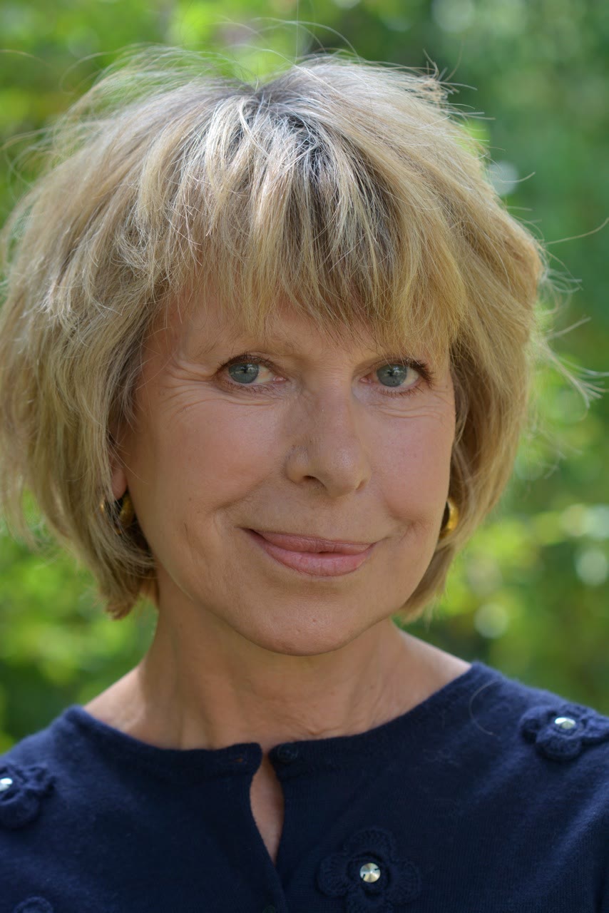 A close-up portrait of a blonde woman wearing a deep navy knit cardigan decorated with crocheted flower appliqués and crystal buttons