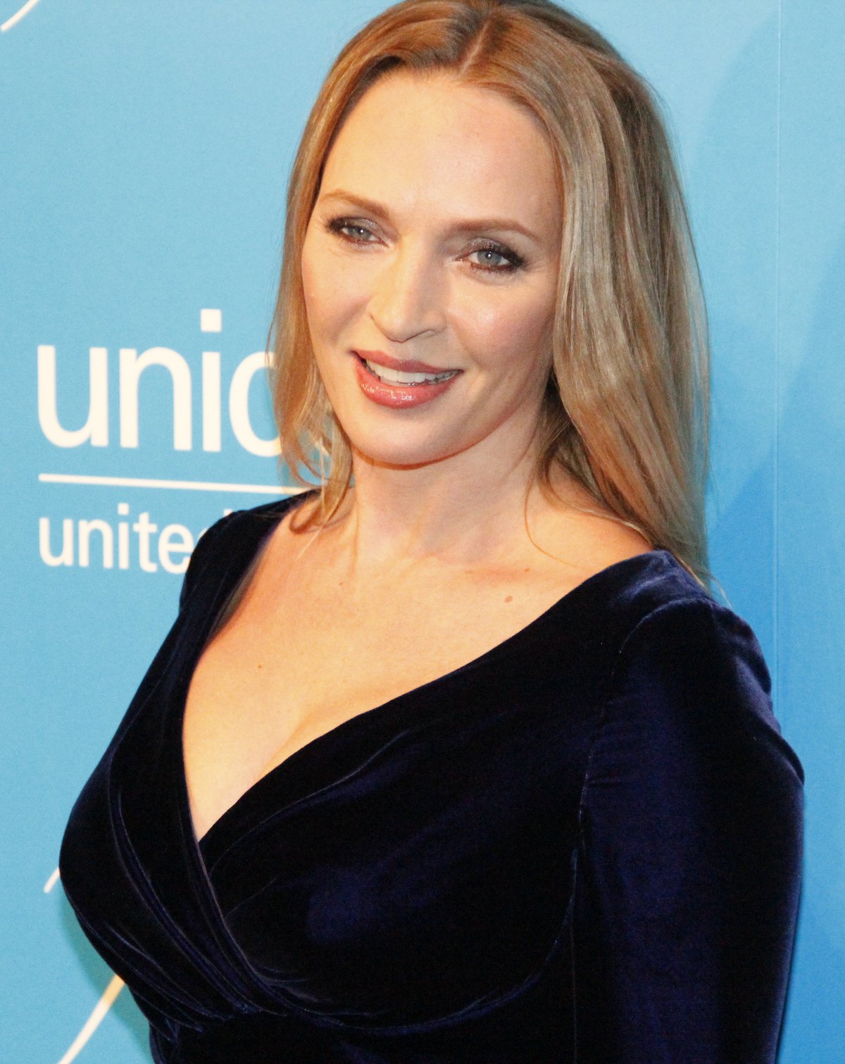 Uma Thurman at a red-carpet event wearing a dark navy velvet wrap-style dress.