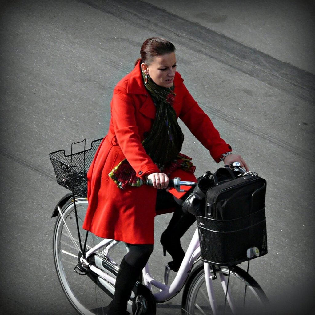 Woman in a bright red coat riding a bicycle, wearing a patterned scarf