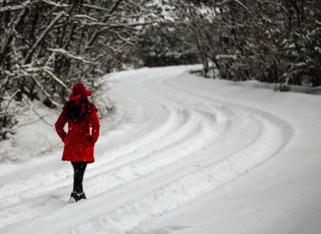 Woman in a red coat and red hat walking along a snow-covered road