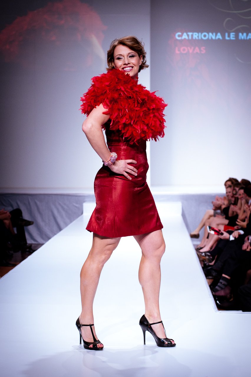 Woman on a runway in a red satin cocktail dress with a dramatic red feather shoulder wrap and black T-strap heels