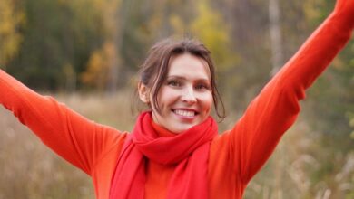 Woman in a red knit sweater and red scarf with her arms raised outdoors