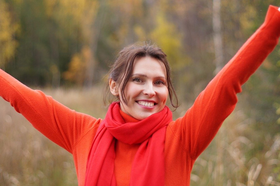 Woman in a red knit sweater and red scarf with her arms raised outdoors