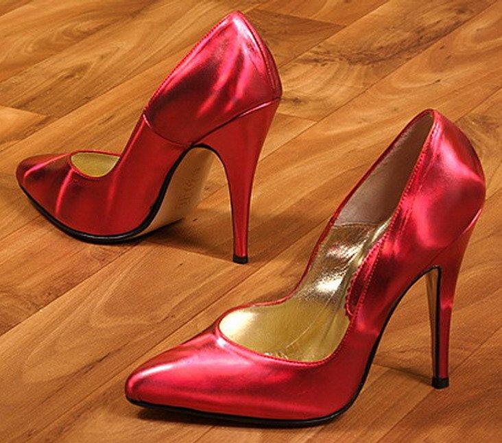 Pair of metallic red pointed-toe stiletto pumps on a wooden floor