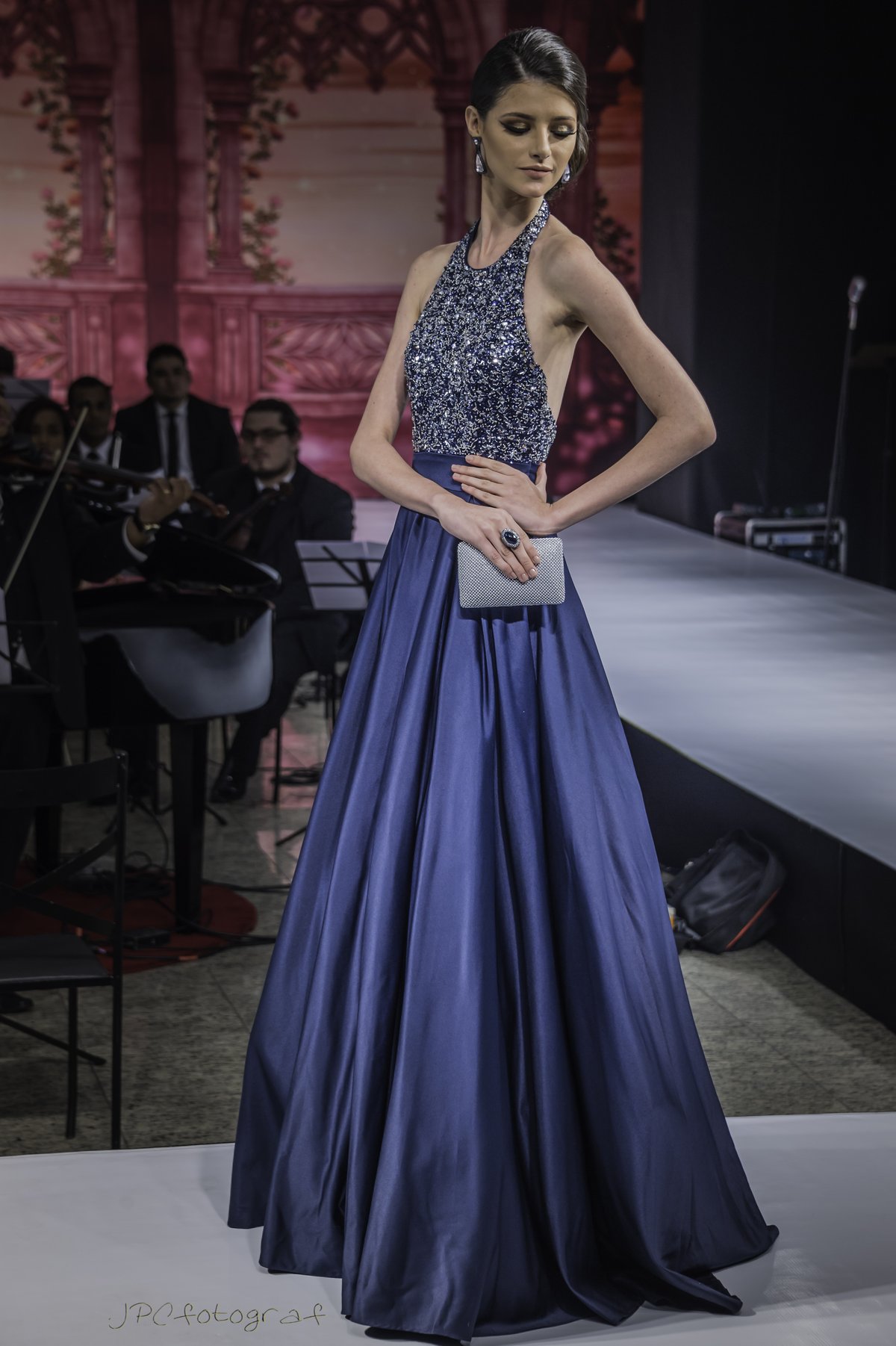 Model wearing a royal blue satin floor-length gown with a sequined halter bodice