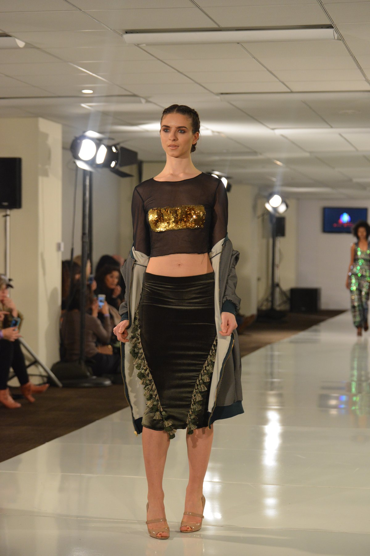 A model on a runway in a gold sequin crop top and a dark green sequin midi skirt