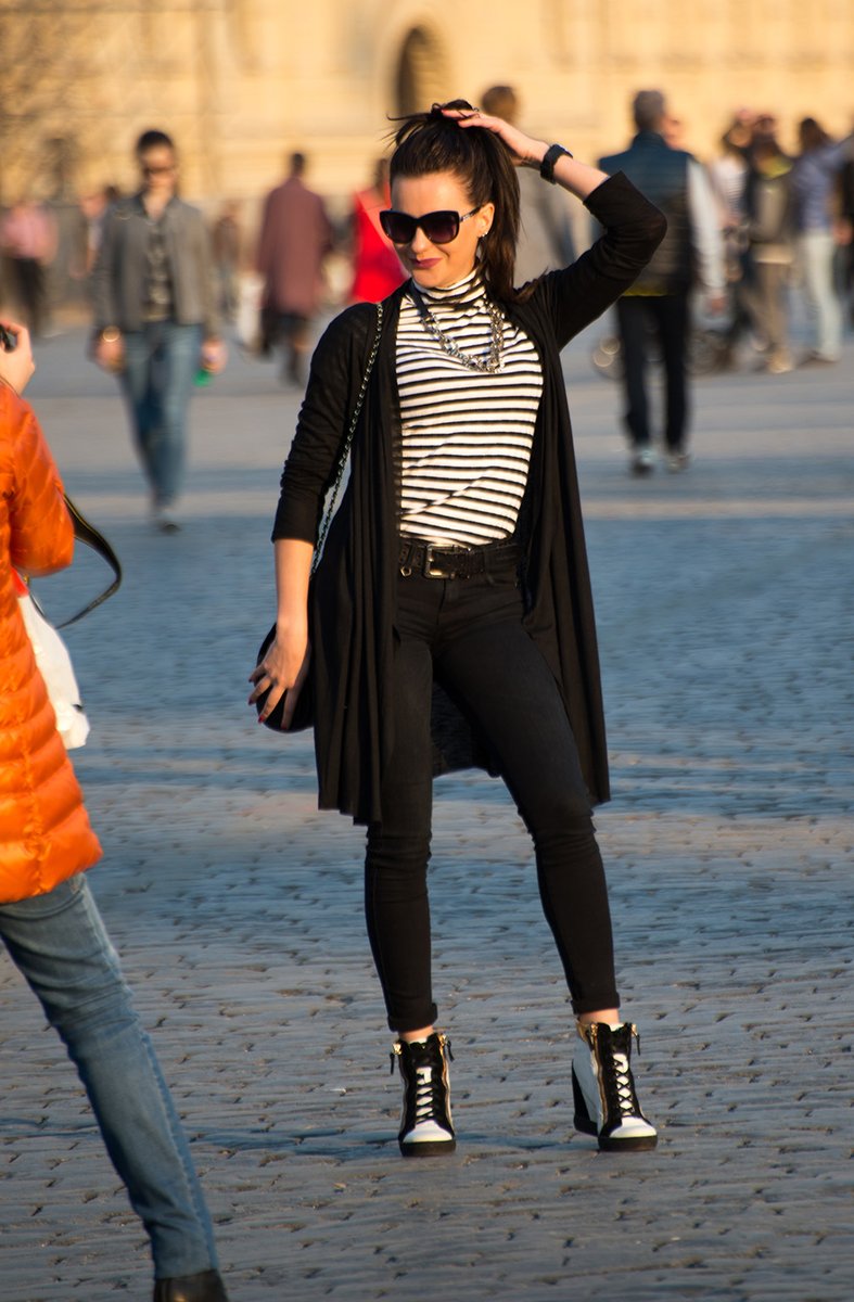 A full-body street-style shot of a woman in a black-and-white striped turtleneck under a long black open duster cardigan with black skinny jeans and lace-up wedge ankle boots