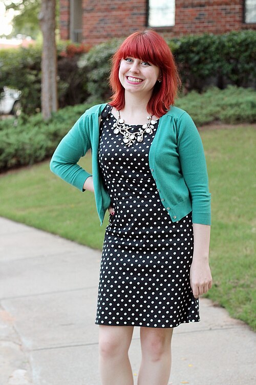 Woman wearing a teal cardigan over a black polka dot shift dress with a statement necklace