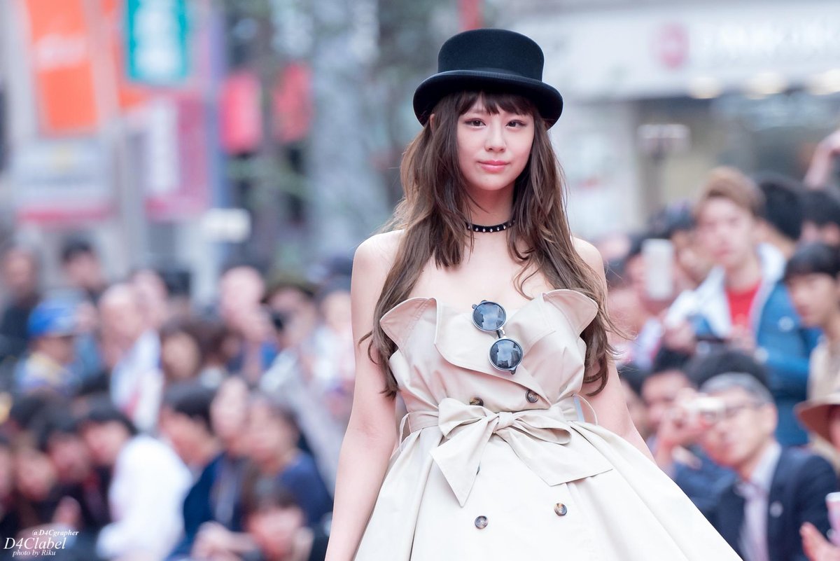 Woman wearing a beige strapless trench-style dress with a bow belt and a black bowler hat