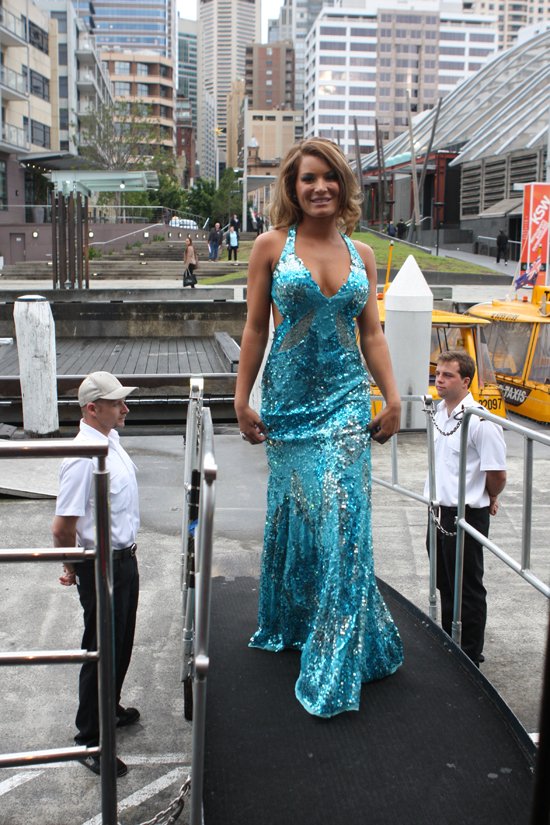 Woman in a sparkling turquoise-blue sequin mermaid evening gown walking outdoors near a waterfront