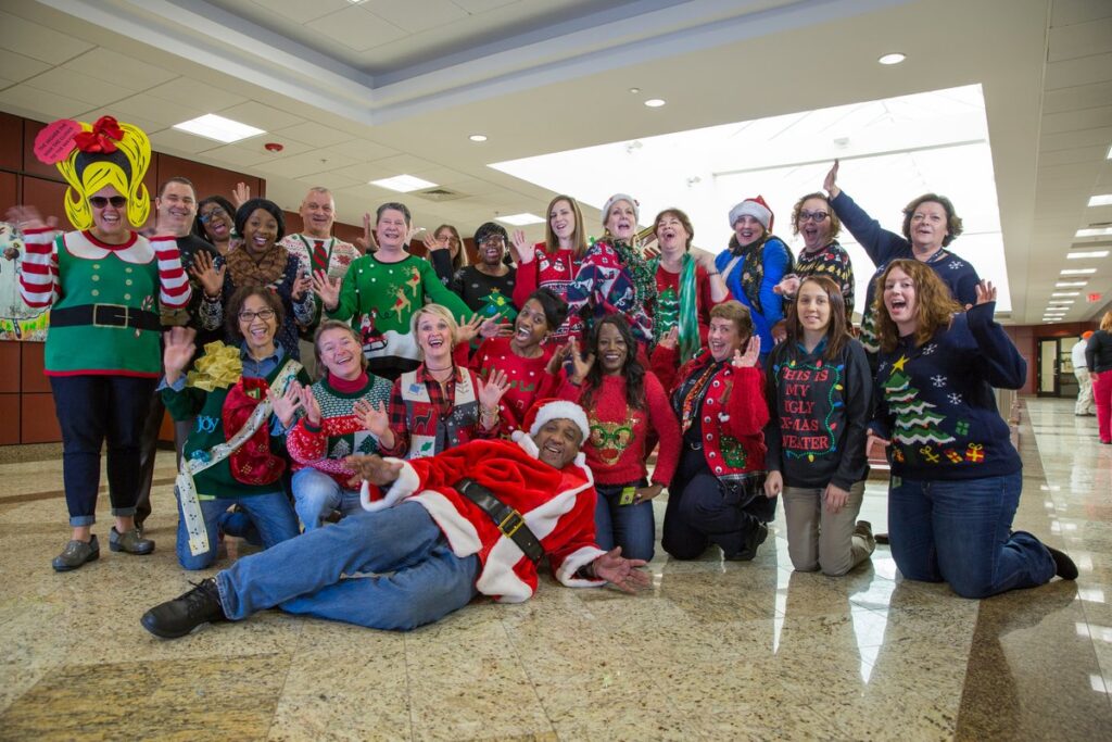 A group of women wearing assorted ugly Christmas sweaters, Santa suits and elf outfits at an office holiday party