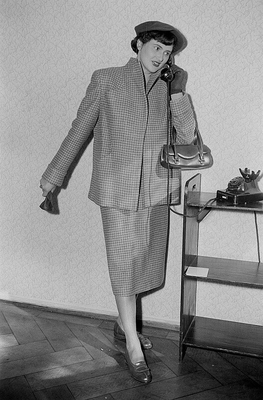 Vintage black-and-white photograph of a woman in a checked skirt suit and beret holding a telephone receiver