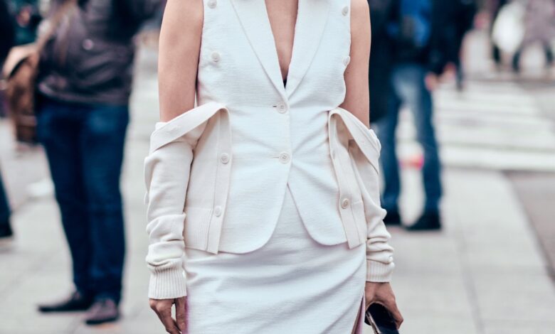 Woman in a white ribbed midi dress and brown knee-high boots walking on a city street