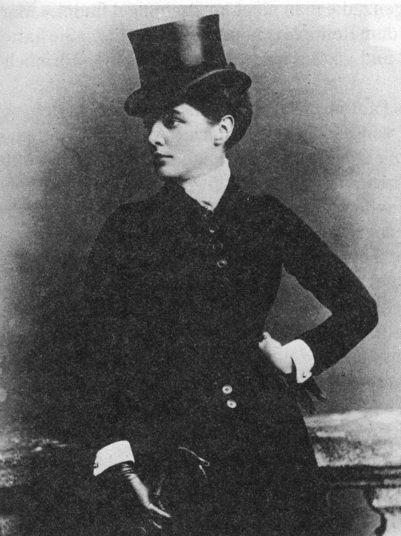 Black-and-white studio portrait of a woman in a black riding jacket with white cuffs and collar, wearing a tall top hat