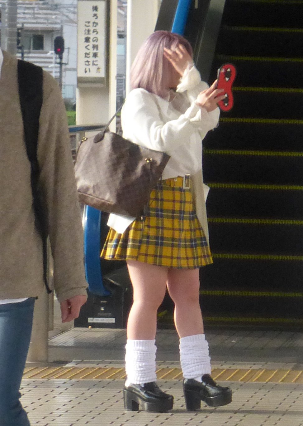 Woman on a Tokyo street wearing a yellow tartan plaid mini skirt with a white sweater, white leg warmers and platform shoes