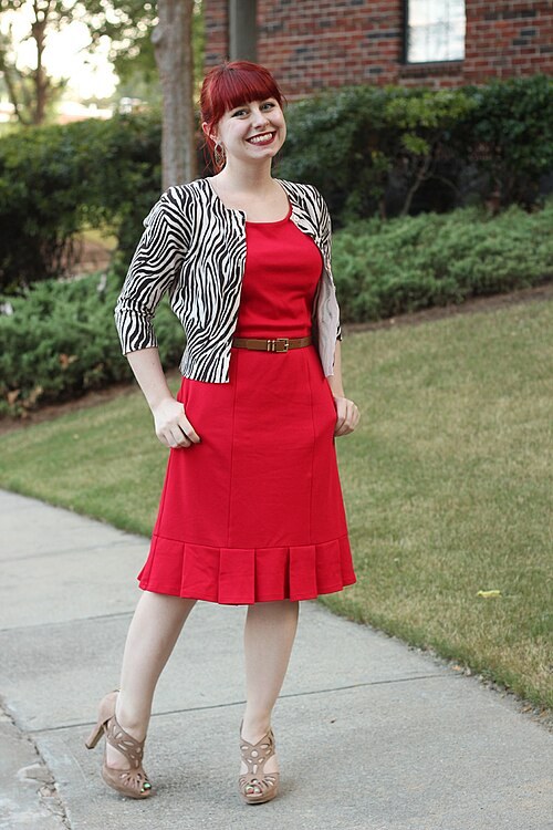 Woman wearing a red fit-and-flare dress with a zebra-print cardigan, brown belt and tan heels